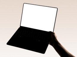 Eine Hand hält einen modernen Laptop vor neutralem Hintergrund – Symbol für flexibles Arbeiten mit Technologie.