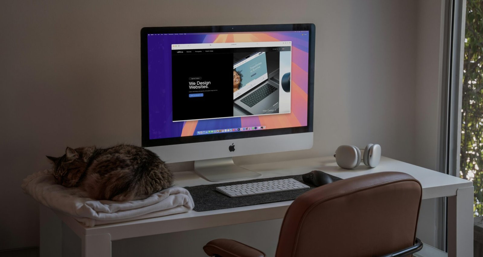 Eine getigerte Katze liegt auf einem Schreibtisch neben einem Computerbildschirm und einer Tastatur.