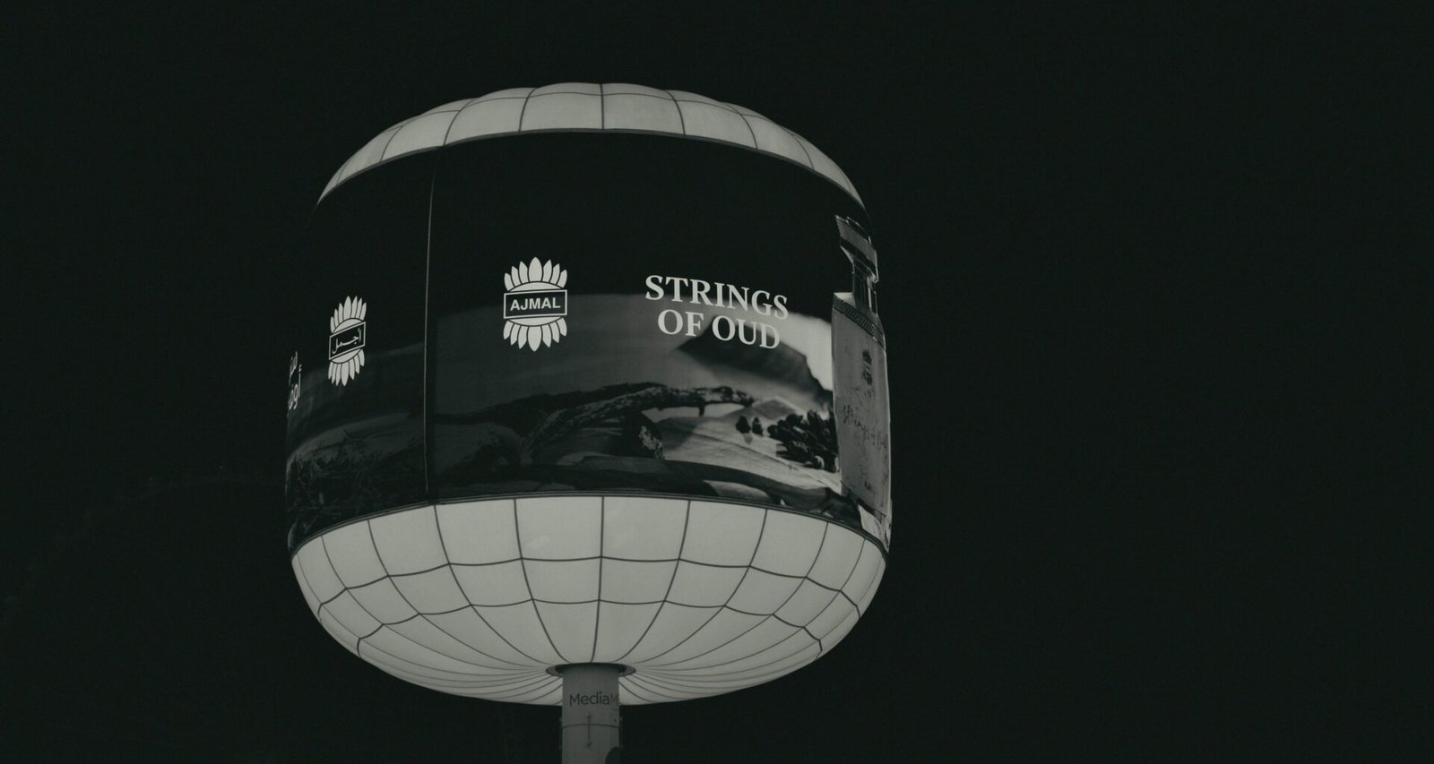 Ein beleuchtetes, kugelförmiges Werbeschild mit der Aufschrift 'strings of old' bei Nacht in urbaner Umgebung.