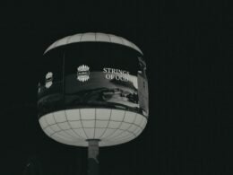 Ein beleuchtetes, kugelförmiges Werbeschild mit der Aufschrift 'strings of old' bei Nacht in urbaner Umgebung.