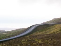 Eine asphaltierte Straße schlängelt sich durch eine grüne, hügelige Gegend mit bewachsenen Hängen