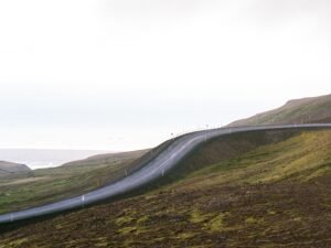Eine asphaltierte Straße schlängelt sich durch eine grüne, hügelige Gegend mit bewachsenen Hängen