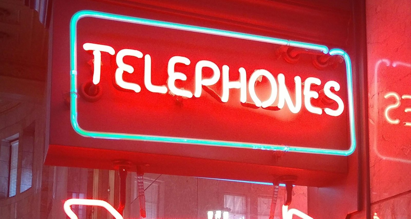 Ein leuchtendes Neon-Schild mit dem Schriftzug „Telephones“, das an der Wand angebracht ist