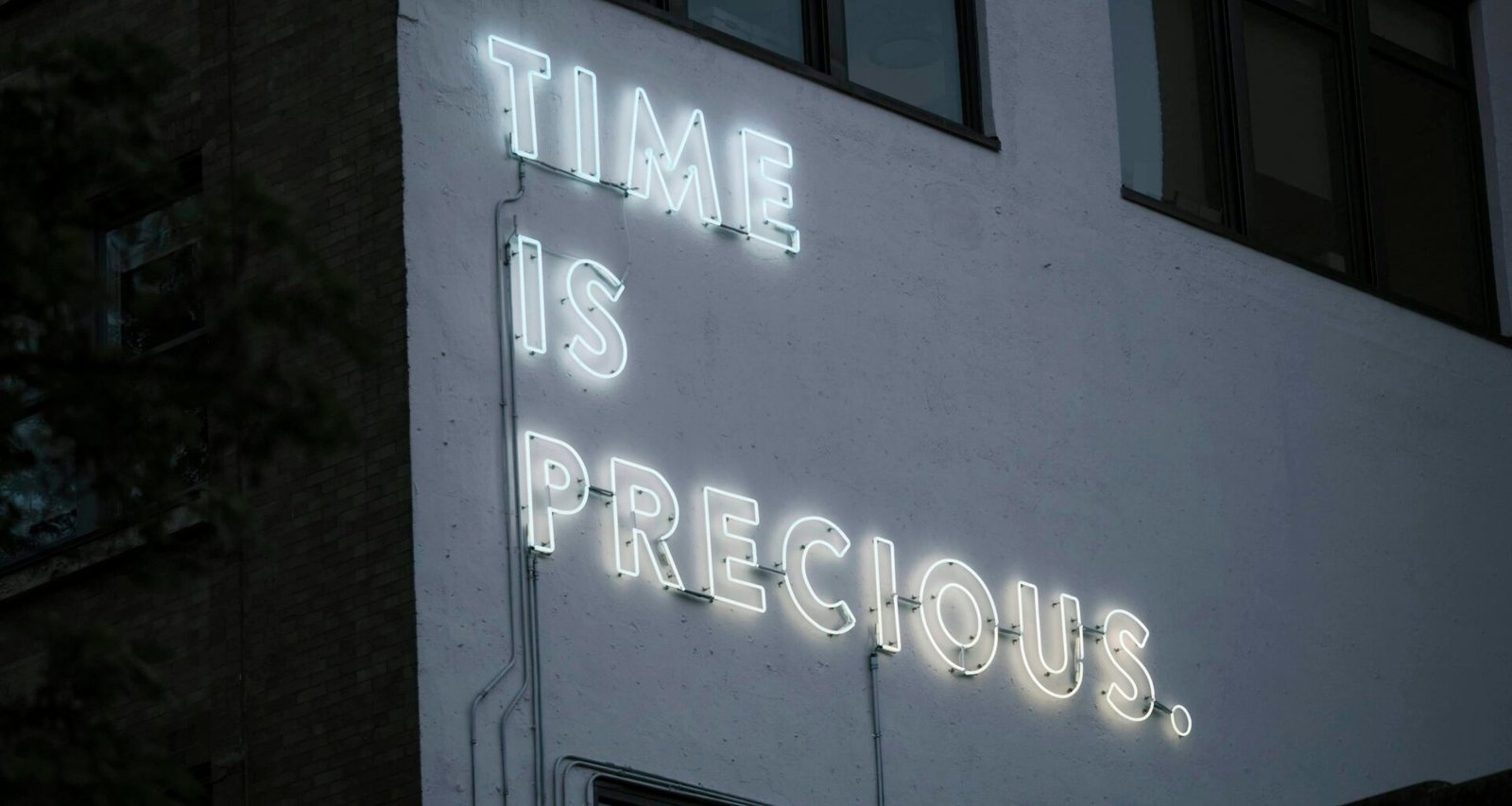 Leuchtendes Neon-Schild mit dem Text Time is precious auf dunklem Hintergrund, fotografiert von Jose Fabula