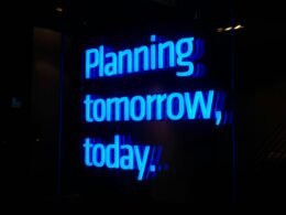 Leuchtender Neon-Schriftzug mit den Worten Planning Tomorrow, Today, fotografiert vor dunklem Hintergrund