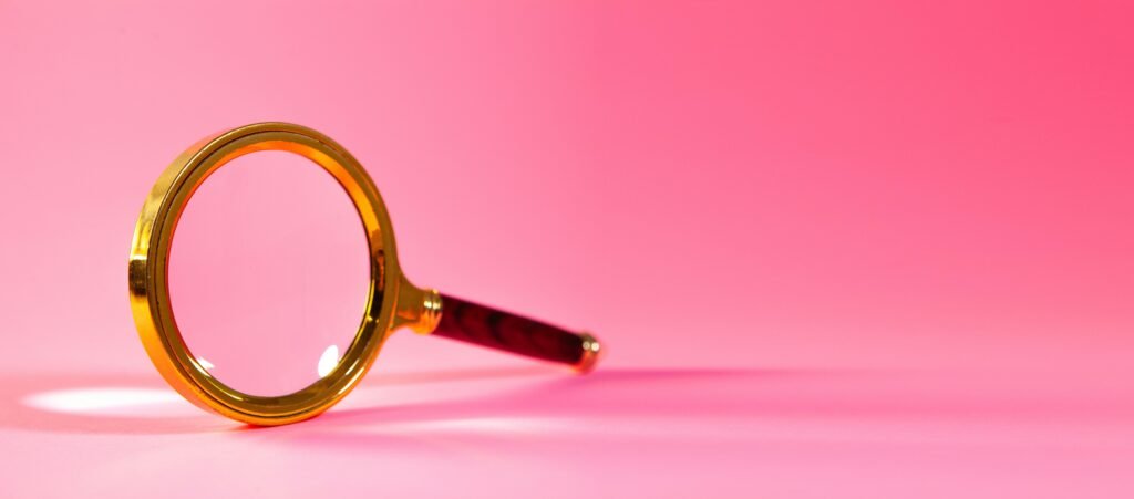 Eine einzelne Lupe liegt auf einem einfarbigen rosa Hintergrund, aufgenommen als Symbolbild für digitale Recherche oder SEO-Themen.