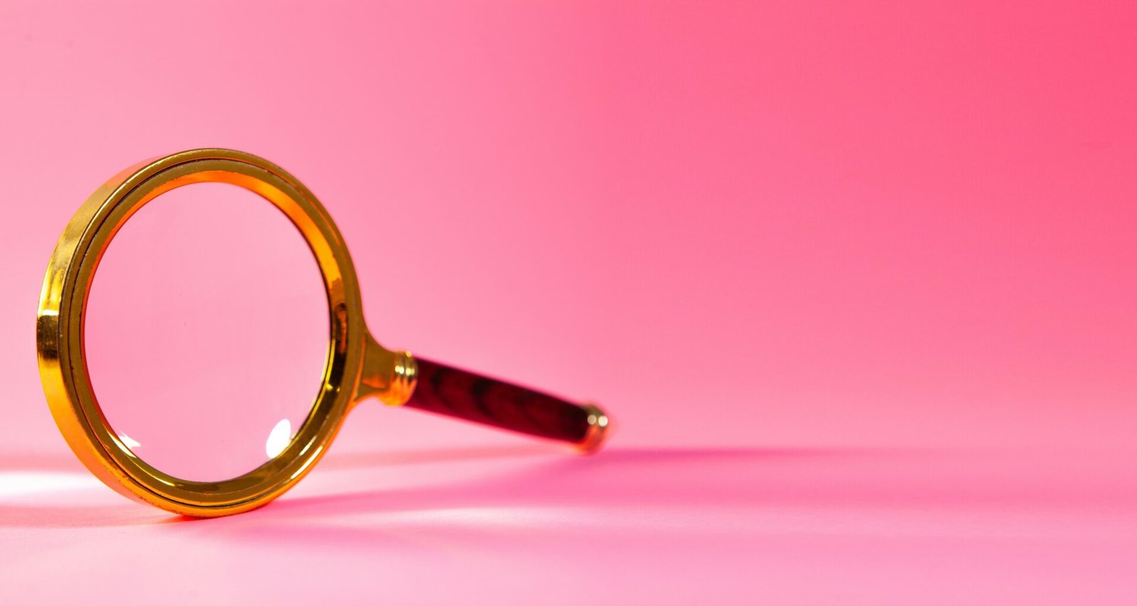 Eine einzelne Lupe liegt auf einem einfarbigen rosa Hintergrund, aufgenommen als Symbolbild für digitale Recherche oder SEO-Themen.