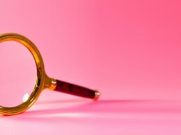Eine einzelne Lupe liegt auf einem einfarbigen rosa Hintergrund, aufgenommen als Symbolbild für digitale Recherche oder SEO-Themen.