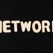 Nahaufnahme des Wortes 'Network' auf einer schwarzen Oberfläche, geeignet für Beiträge zu Technologie und digitalen Netzwerken