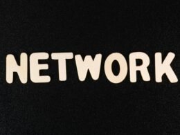 Nahaufnahme des Wortes 'Network' auf einer schwarzen Oberfläche, geeignet für Beiträge zu Technologie und digitalen Netzwerken