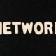 Nahaufnahme des Wortes 'Network' auf einer schwarzen Oberfläche, geeignet für Beiträge zu Technologie und digitalen Netzwerken
