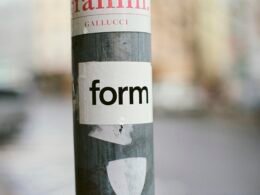 Detailansicht eines Pfostens mit aufgeklebtem Sticker im urbanen Umfeld vor unscharfem Hintergrund