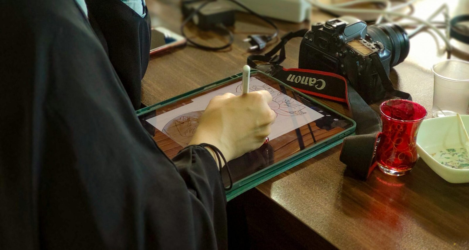 Eine Person sitzt an einem Schreibtisch und schreibt mit einem Stift auf einem Tablet in einer modernen Arbeitsumgebung.