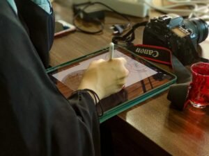 Eine Person sitzt an einem Schreibtisch und schreibt mit einem Stift auf einem Tablet in einer modernen Arbeitsumgebung.
