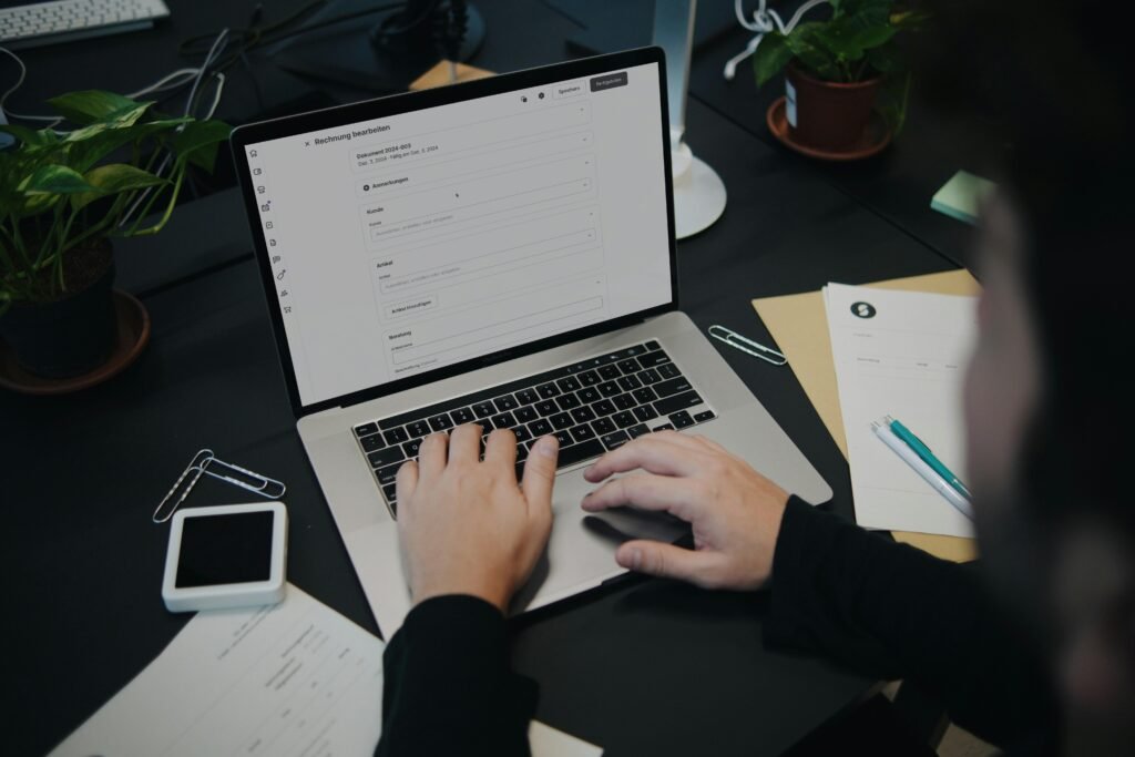 Person sitzt an einem Schreibtisch und nutzt einen Laptop Computer zur Arbeit in einer modernen Büroumgebung.