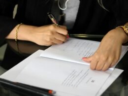 Person hält einen Stift und schreibt Notizen auf ein Blatt Papier, Nahaufnahme der Hand und des Schreibprozesses