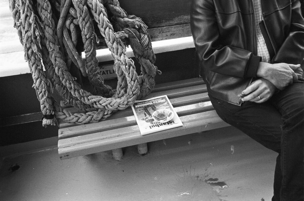 Eine Person sitzt auf einer Bank im Freien und liest eine gefaltete Zeitung, die beide Hände umfasst.