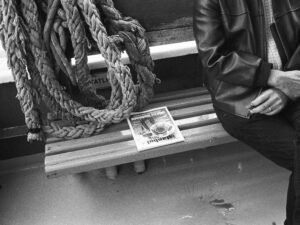 Eine Person sitzt auf einer Bank im Freien und liest eine gefaltete Zeitung, die beide Hände umfasst.