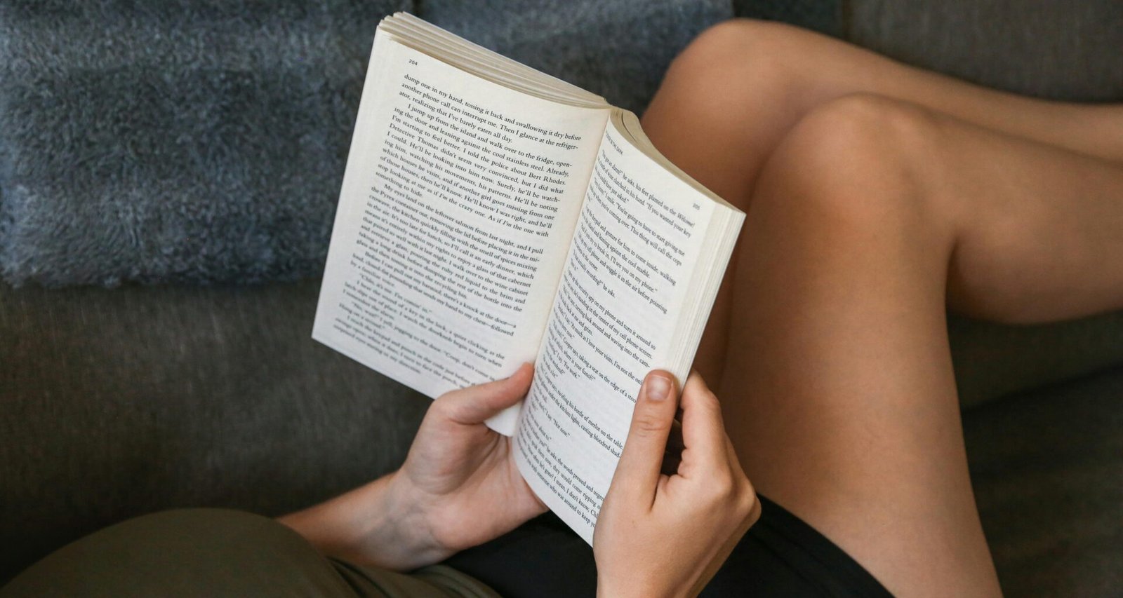 Person liegt auf einer Couch und liest ein Buch in entspannter Umgebung, modernes Wohnzimmer, natürliche Lichtverhältnisse