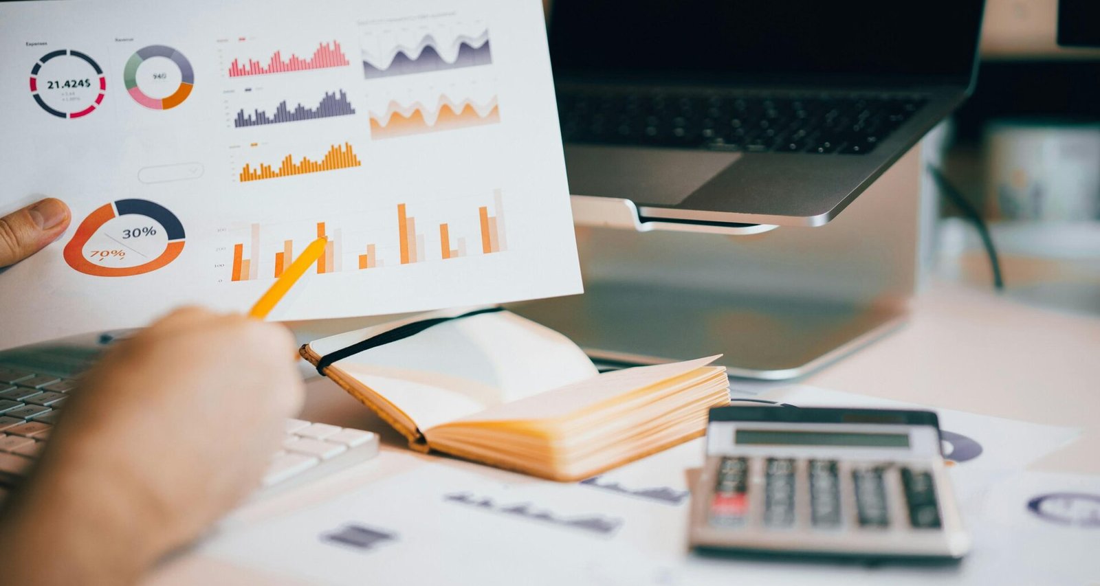 Eine Person hält ein Blatt Papier über die Tastatur eines aufgeklappten Laptops auf einem Schreibtisch.