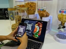 Person arbeitet am Tisch gleichzeitig mit einem Smartphone und einem Laptop, beide Geräte nebeneinander platziert