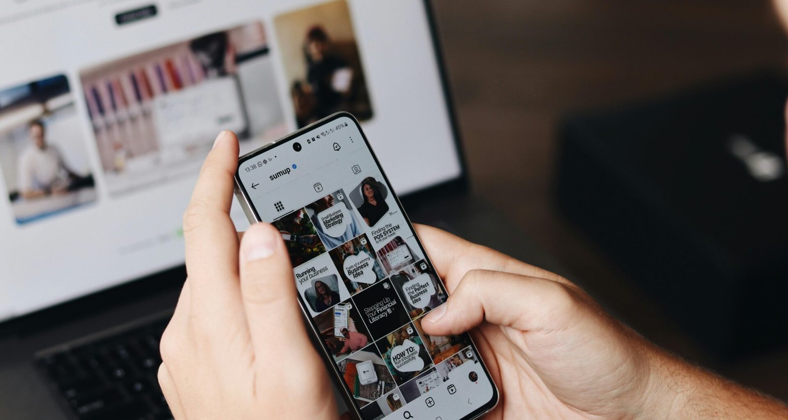 Eine Person hält ein Smartphone vor einen geöffneten Laptop, beide Geräte werden gleichzeitig genutzt