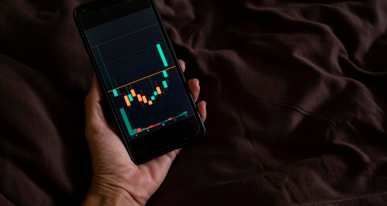 Eine Person hält ein Smartphone mit einem Balkendiagramm auf dem Bildschirm, das Datenanalyse oder Statistiken darstellt.