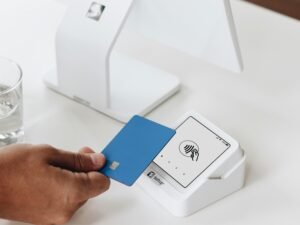 Eine Person hält eine Bankkarte vor einen Laptop, um eine Online-Zahlung oder digitale Transaktion durchzuführen.