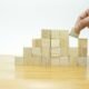 Eine Person legt einen Holzblock auf einen Stapel aus Holzklötzen, als Symbol für Strategie und Aufbau im digitalen Kontext.