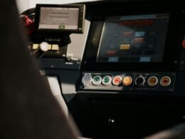 Eine Person sitzt in einem Fahrzeug und nutzt ein übersichtliches Kontrollpanel mit verschiedenen Bedienelementen.