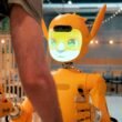 Eine Person steht einem orangefarbenen Roboter gegenüber und interagiert mit ihm in einer modernen Umgebung.