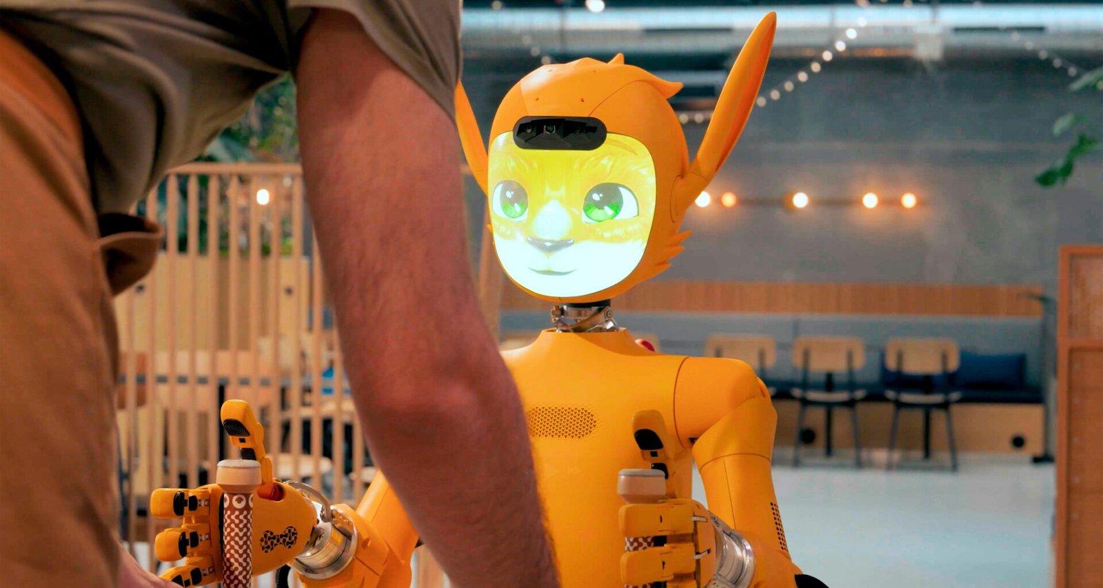 Eine Person steht einem orangefarbenen Roboter gegenüber und interagiert mit ihm in einer modernen Umgebung.