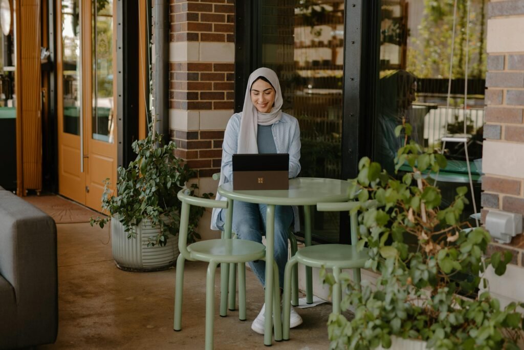 Person sitzt an einem Tisch und nutzt einen Laptop für digitale Arbeit, modernes Umfeld mit Technik am Arbeitsplatz.