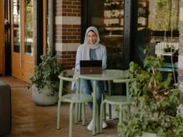 Person sitzt an einem Tisch und nutzt einen Laptop für digitale Arbeit, modernes Umfeld mit Technik am Arbeitsplatz.