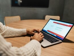 Eine Person arbeitet an einem Tisch mit aufgeklapptem Laptop und konzentriert sich auf den Bildschirm