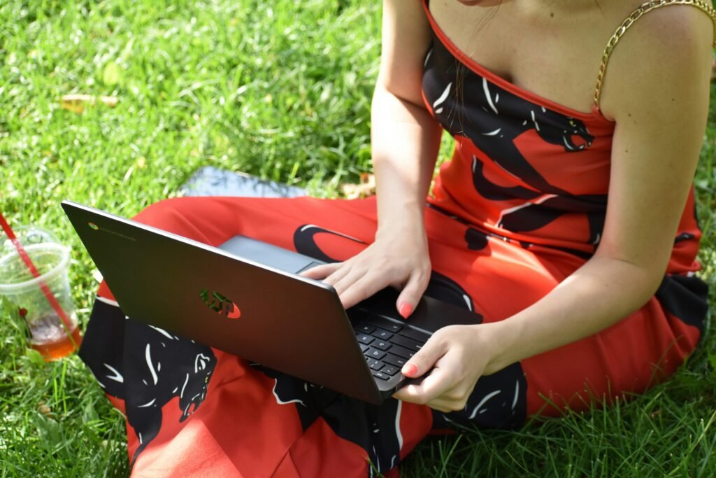 Eine Person sitzt entspannt auf einer Wiese und nutzt einen Laptop für die Arbeit oder Freizeit im Freien.