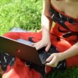 Eine Person sitzt entspannt auf einer Wiese und nutzt einen Laptop für die Arbeit oder Freizeit im Freien.