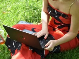 Eine Person sitzt entspannt auf einer Wiese und nutzt einen Laptop für die Arbeit oder Freizeit im Freien.