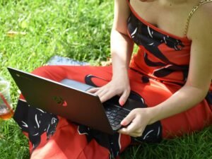 Eine Person sitzt entspannt auf einer Wiese und nutzt einen Laptop für die Arbeit oder Freizeit im Freien.