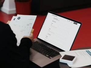 Person an einem Schreibtisch mit Laptop, Notizen und Dokumenten, vertieft in die Arbeit – modernes Arbeitsumfeld