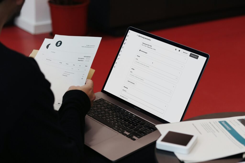 Person arbeitet an einem Schreibtisch mit Laptop und Papieren, Organisation und digitale Tools stehen im Mittelpunkt.