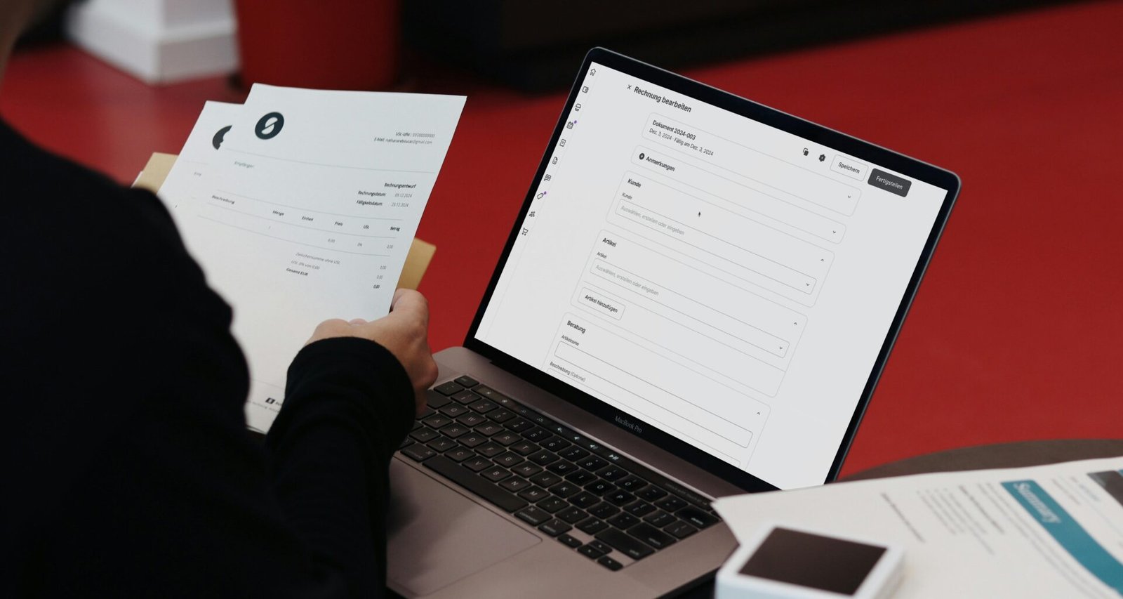 Person sitzt an einem Schreibtisch mit einem Laptop und Papierdokumenten, arbeitet fokussiert an Projekten