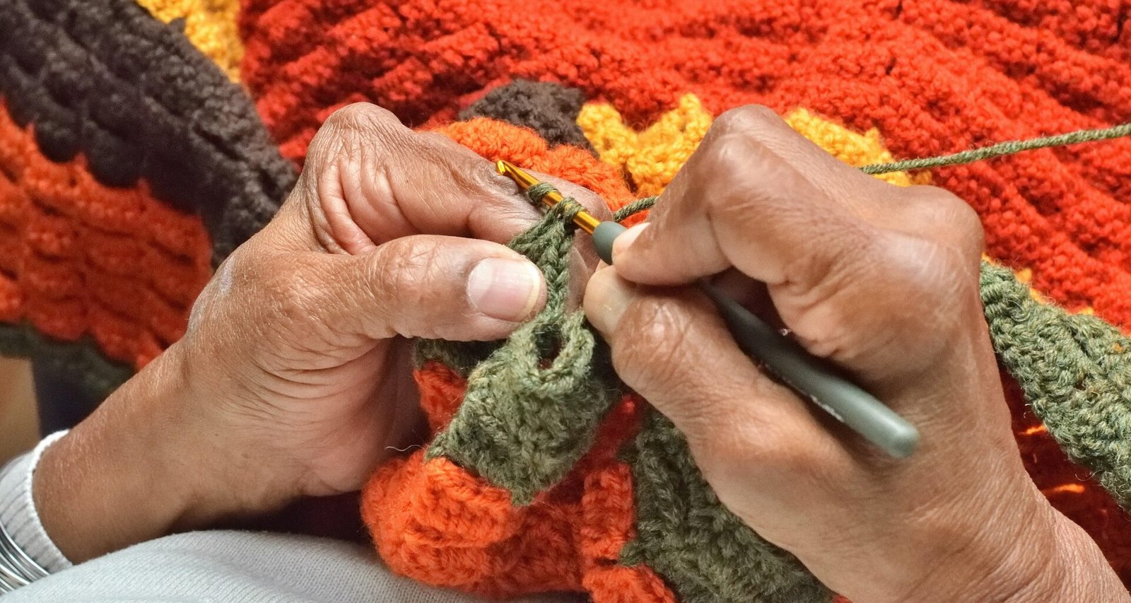 Person beim Stricken einer Decke mit Wolle und einer Schere, Fokus auf die Hände und das Strickmaterial