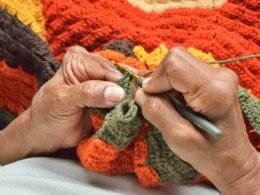 Person beim Stricken einer Decke mit Wolle und einer Schere, Fokus auf die Hände und das Strickmaterial