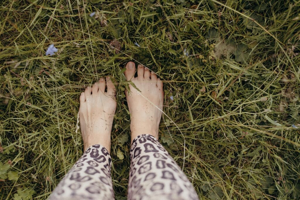 Eine Person steht mit den Füßen nach oben im grünen Gras, Fokus auf die Beine und die natürliche Umgebung