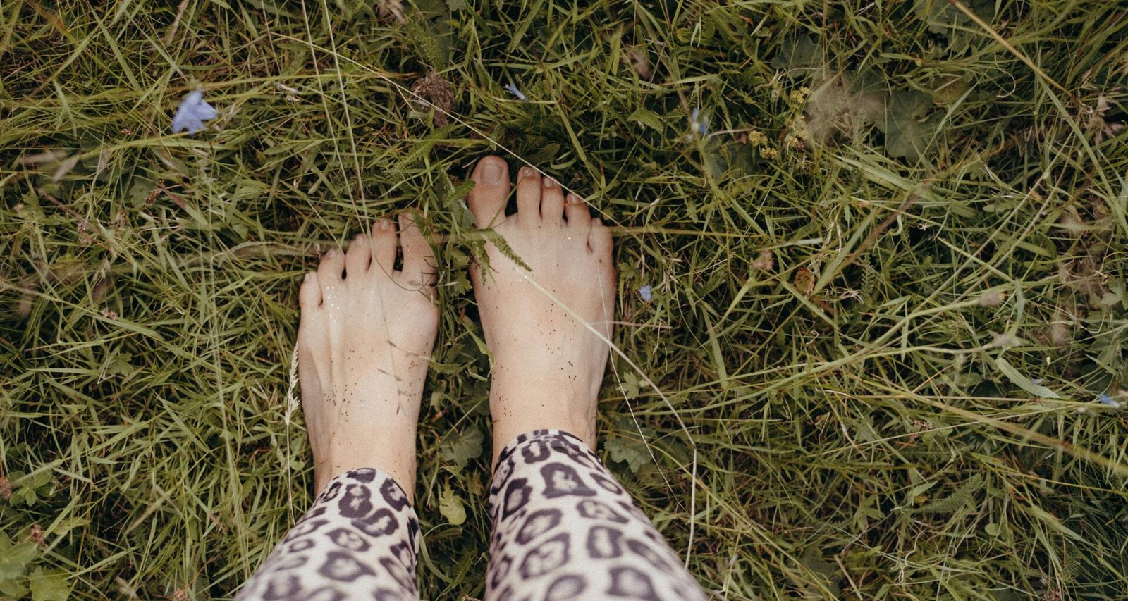 Eine Person steht mit den Füßen nach oben im grünen Gras, Fokus auf die Beine und die natürliche Umgebung