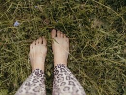 Eine Person steht mit den Füßen nach oben im grünen Gras, Fokus auf die Beine und die natürliche Umgebung