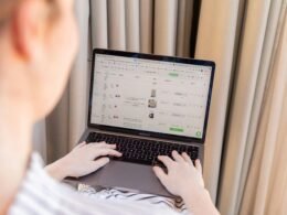 Eine Person sitzt vor einem Laptop an einem Schreibtisch in moderner Umgebung und arbeitet konzentriert.