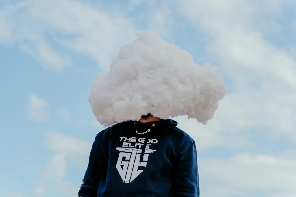 Eine Person steht vor neutralem Hintergrund, der Kopf wird von einer großen weißen Wolke verdeckt dargestellt.