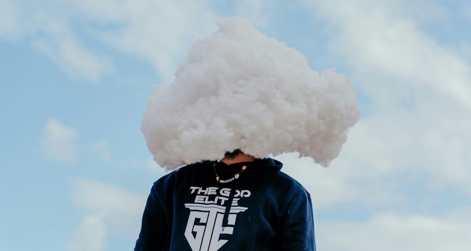 Eine Person steht vor neutralem Hintergrund, der Kopf wird von einer großen weißen Wolke verdeckt dargestellt.